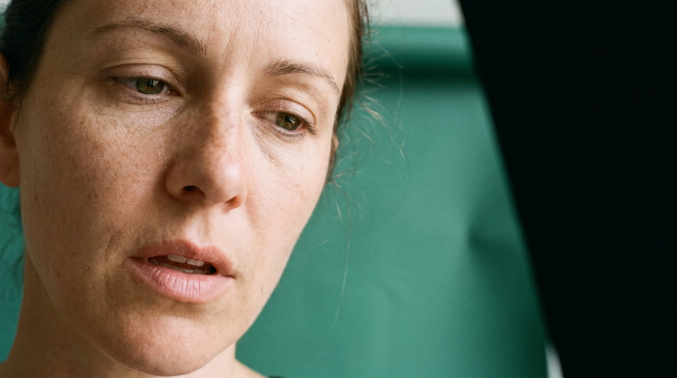 A woman photographed close on verdigris seamless, eyes down, in the moment just after letting a breath go.