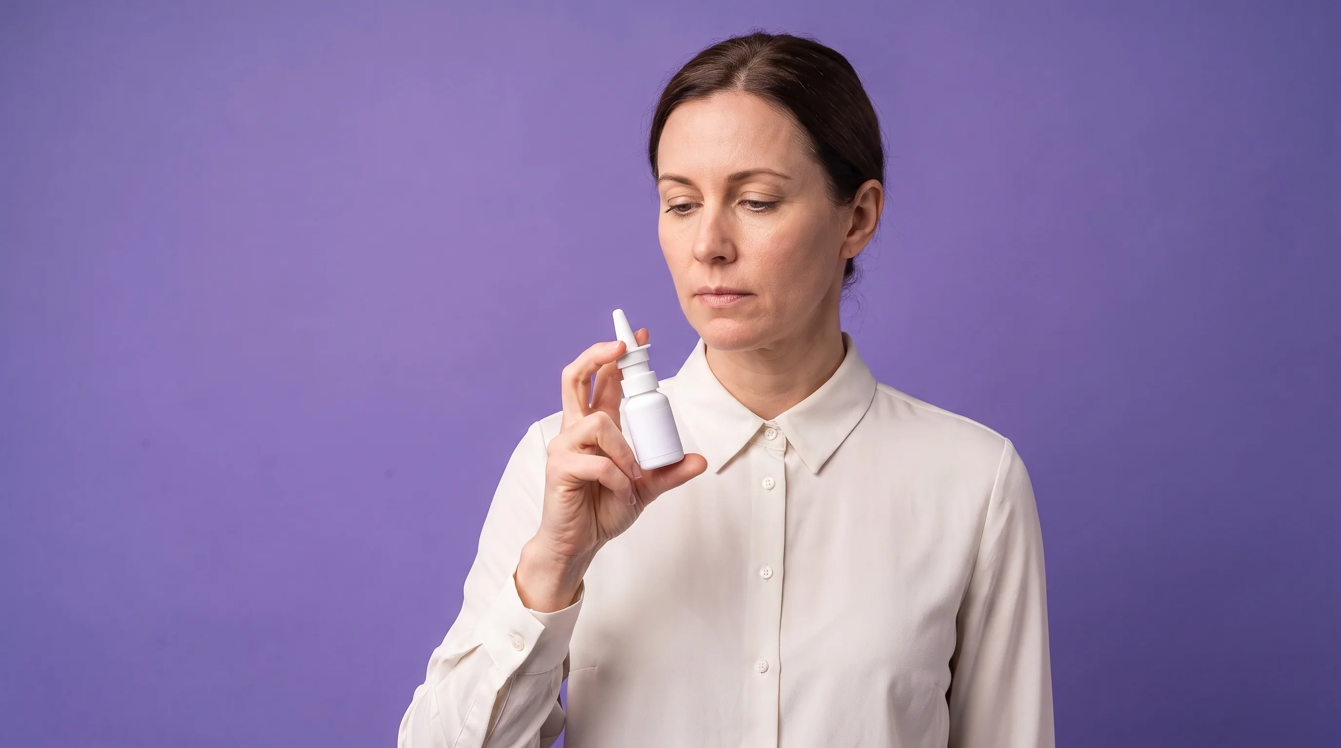A woman priming the nasal sprayer, looking down at the nozzle