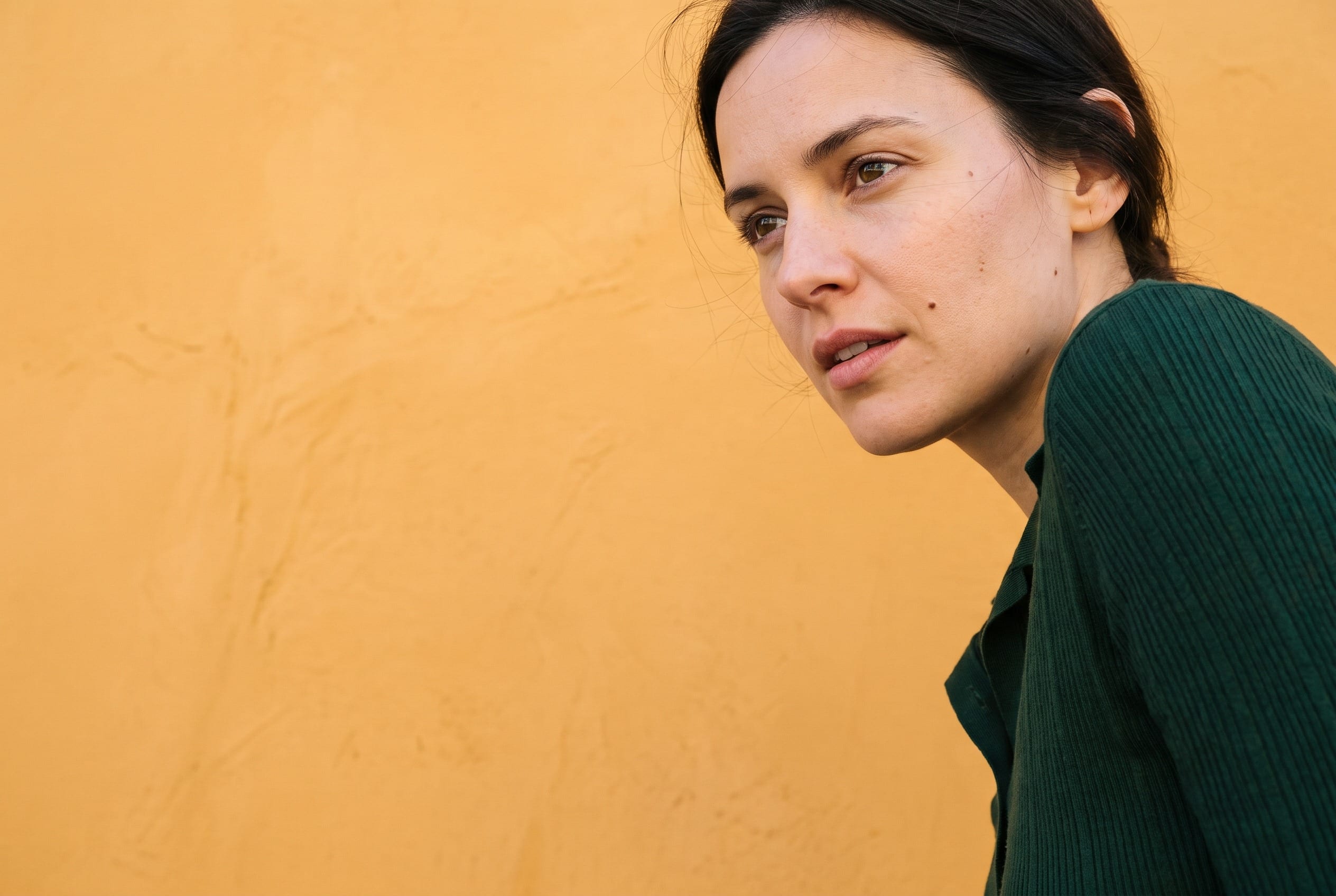 A woman turning back toward the camera against an amber plaster wall.