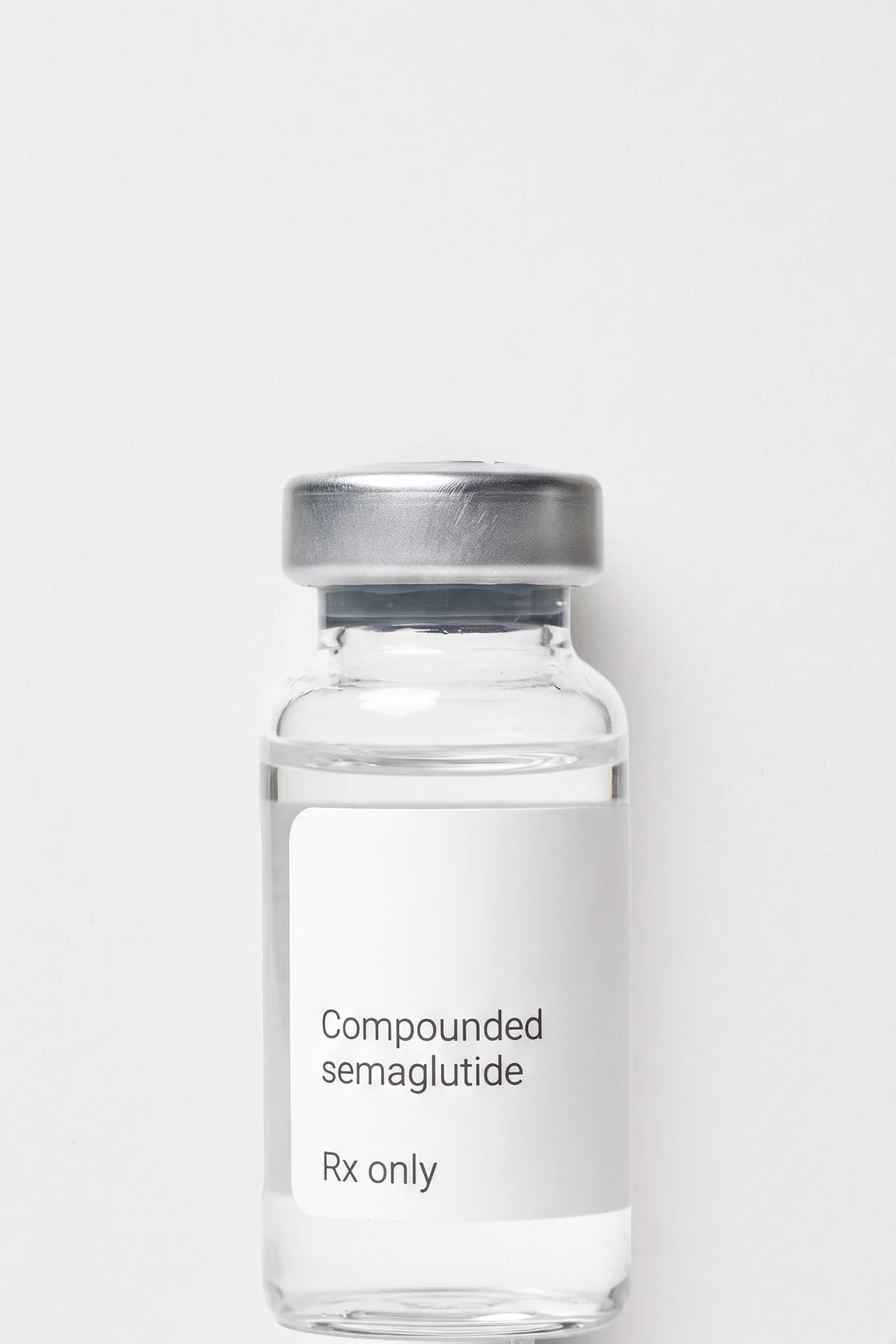 A vial of compounded semaglutide standing on a flat near-white ground