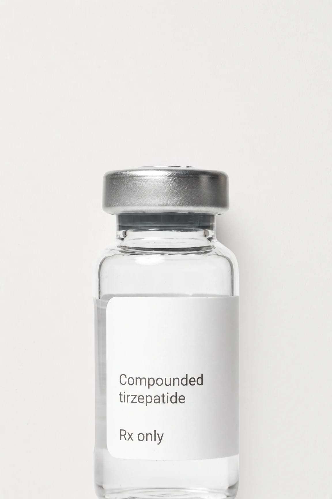 A vial of compounded tirzepatide standing on a flat near-white ground