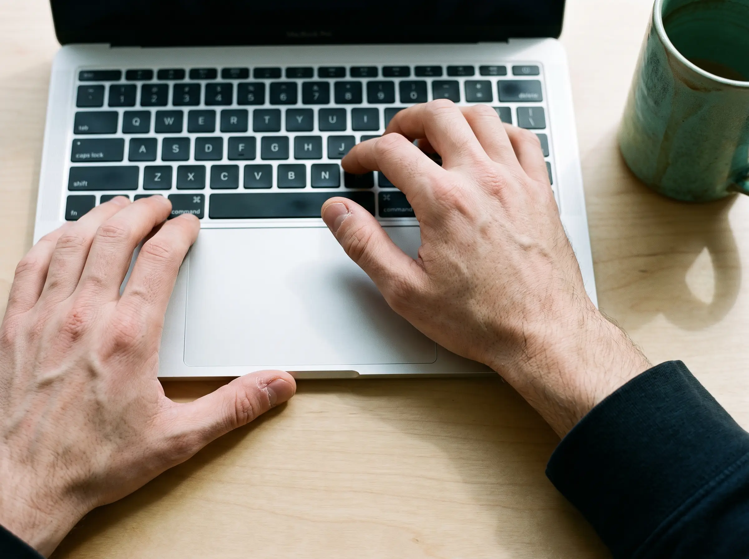 Two hands at a laptop keyboard, mid-reply, a mug at the edge of the desk.