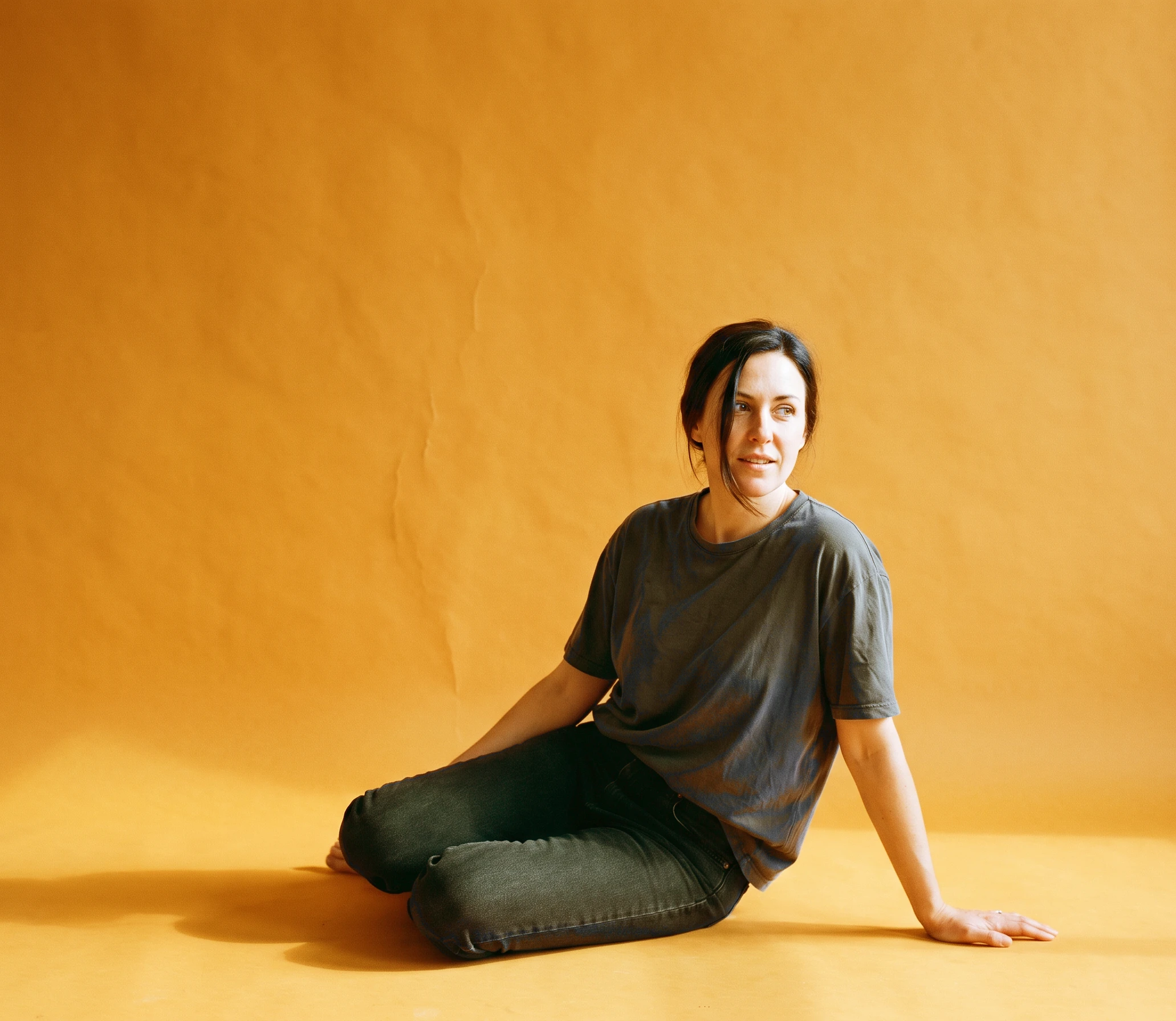 A woman sitting on the floor of an amber seamless paper cove