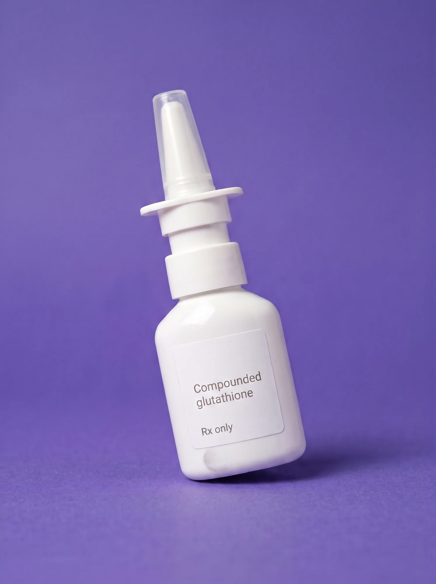 A plain white nasal spray bottle labelled Compounded glutathione, Rx only, standing at an angle on iris paper