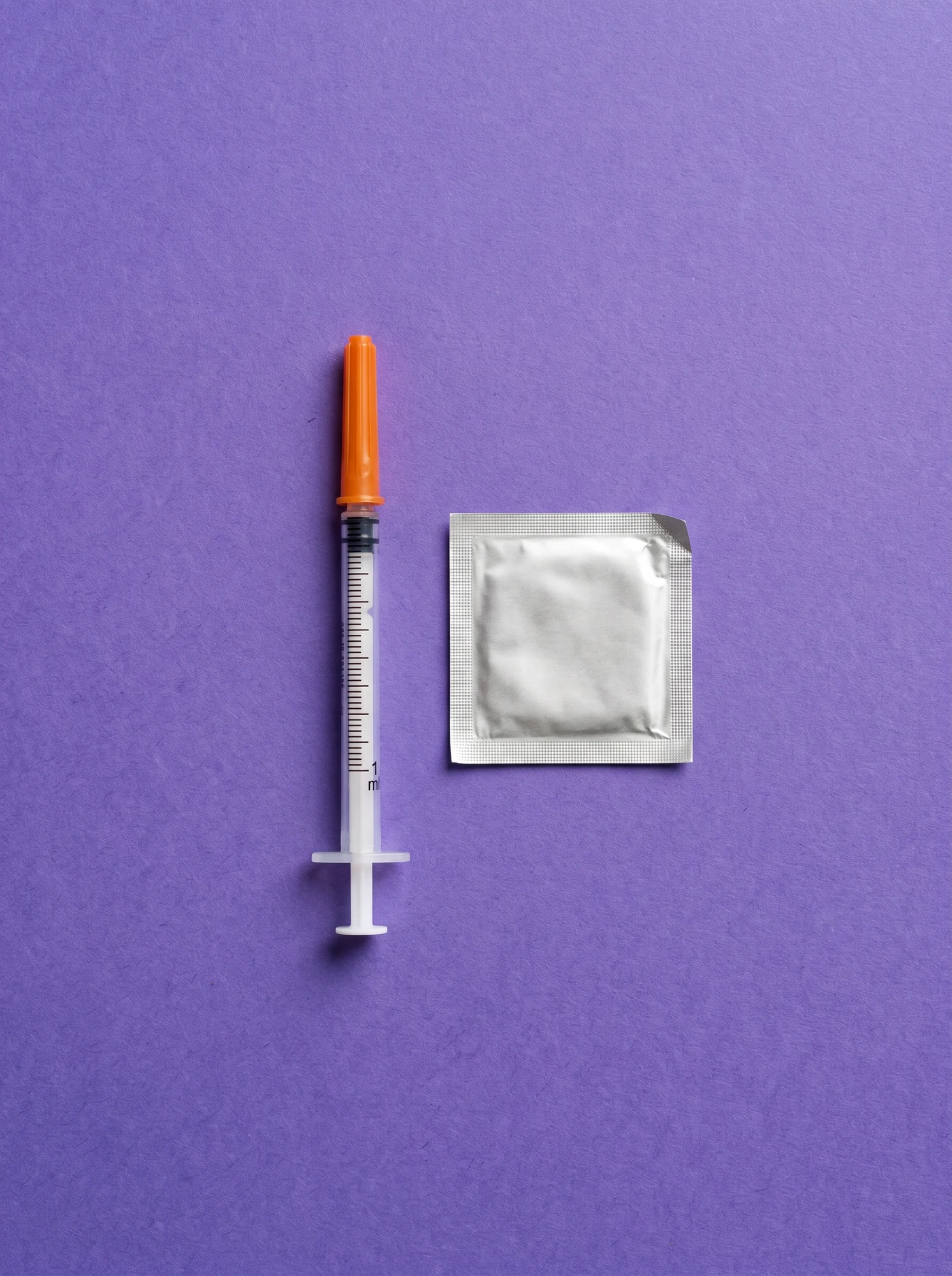 A capped syringe and a sealed alcohol swab laid parallel on iris paper