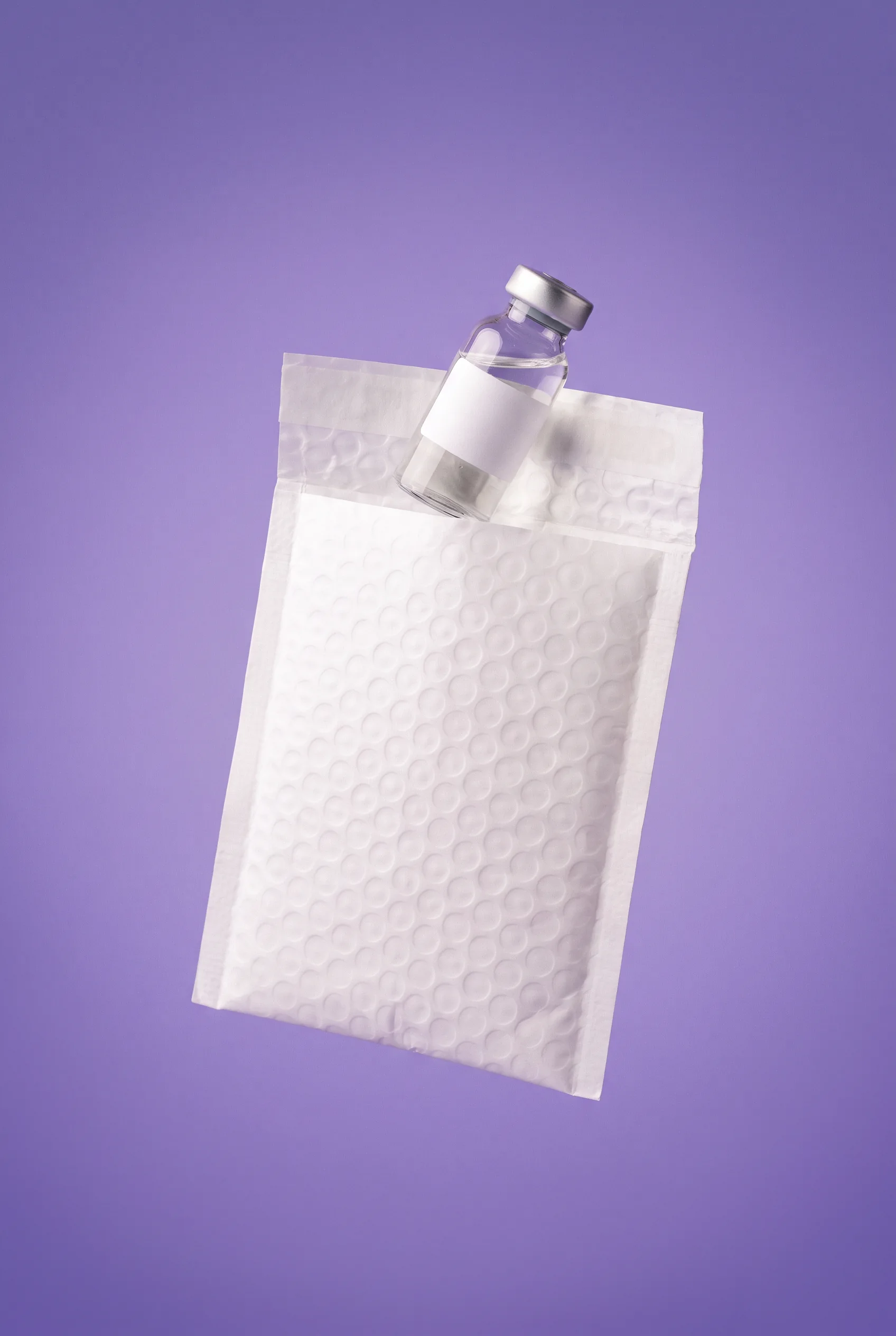 A plain white mailer floating open with one unlabelled vial emerging from it, iris ground