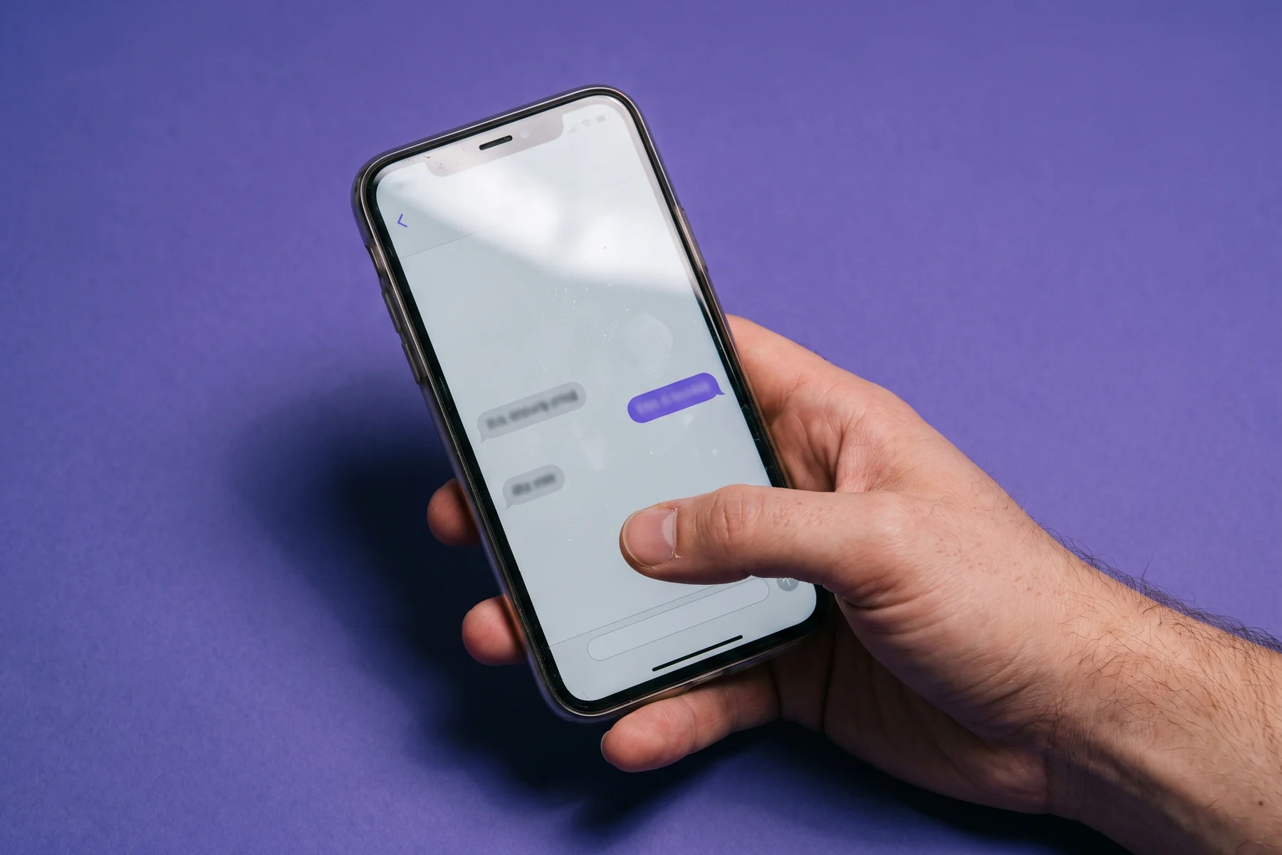 A hand holding a phone showing a secure message thread, against iris paper