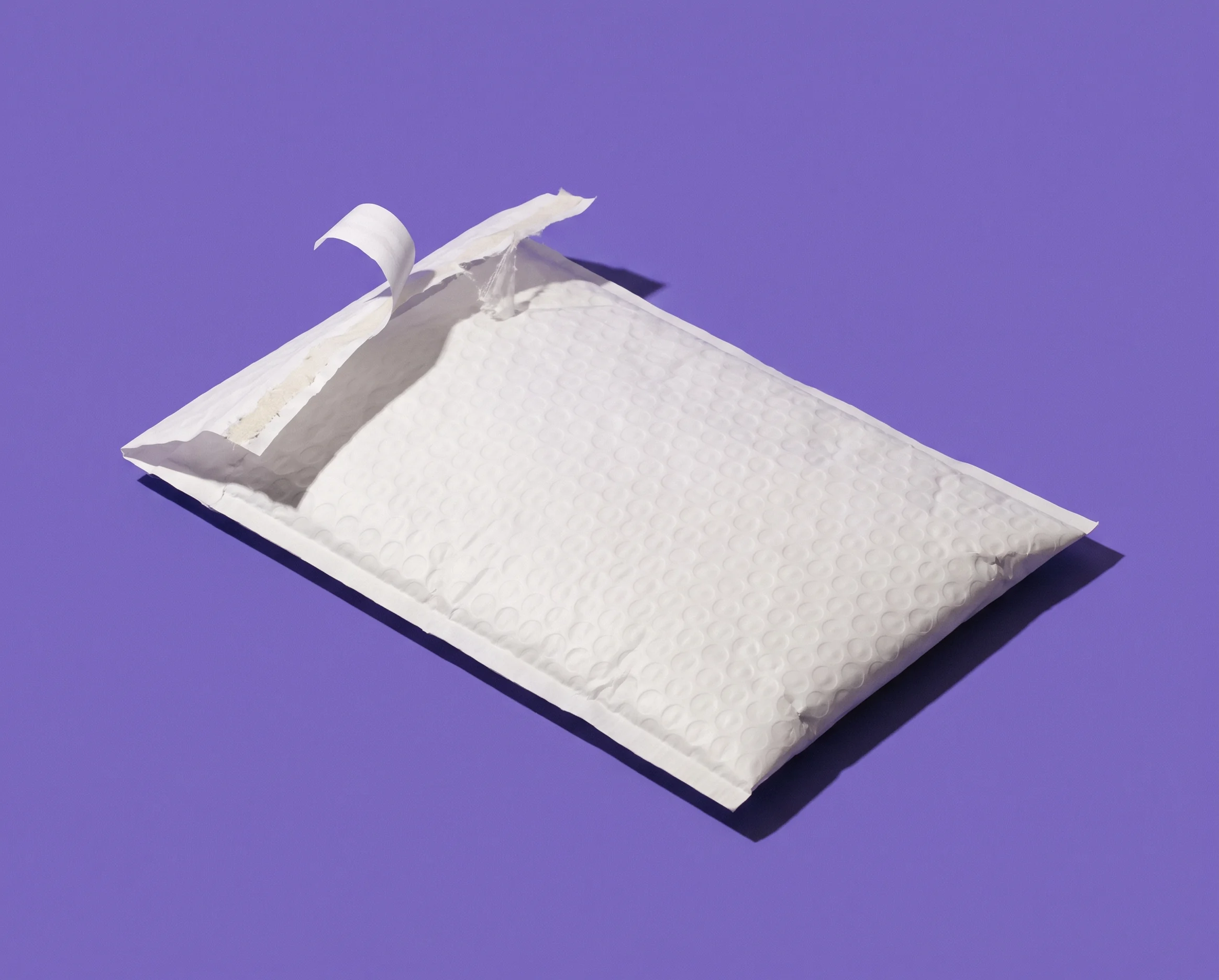 An unlabelled padded mailer laid flat on iris paper with one corner lifted