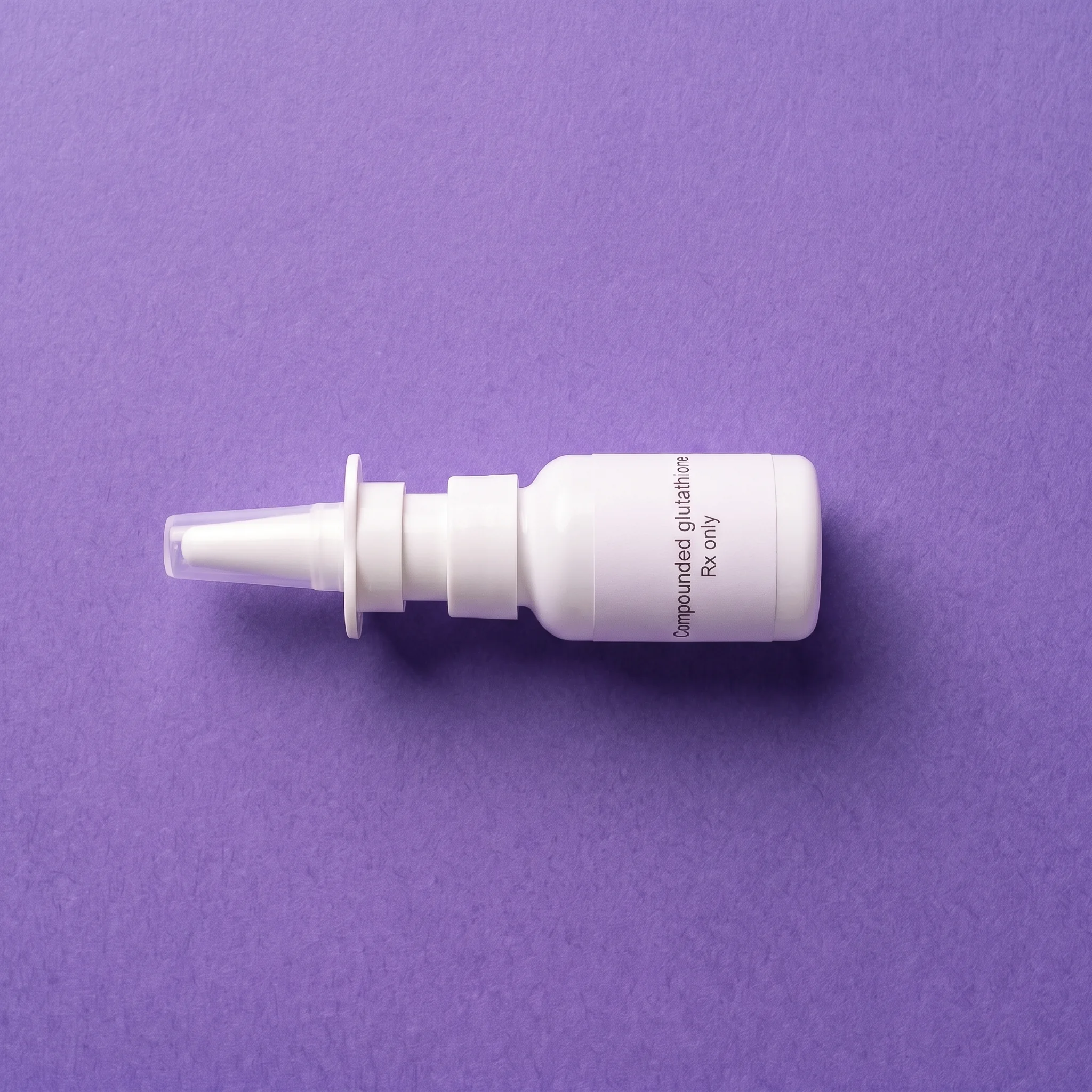 The Compounded glutathione sprayer bottle laid on its side on iris paper