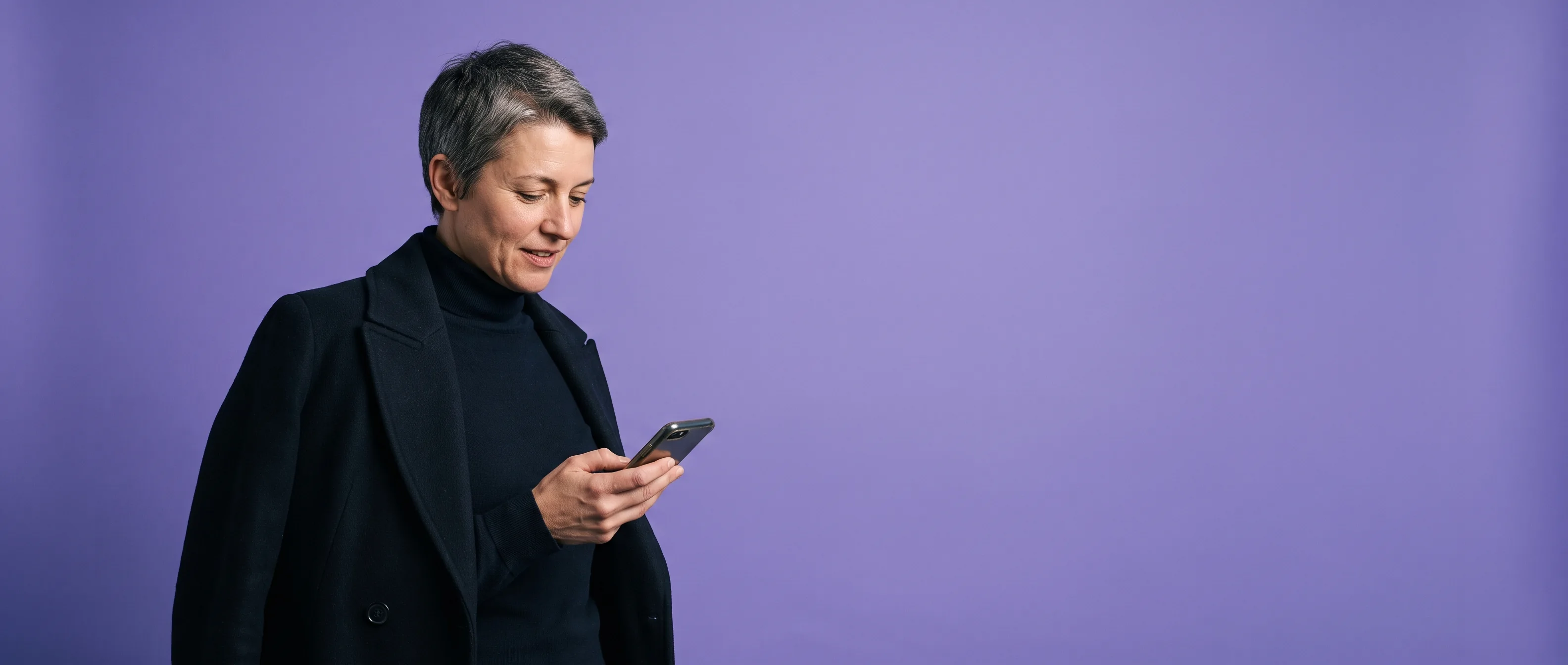 A woman with her coat still on, paused to read her phone, against iris paper