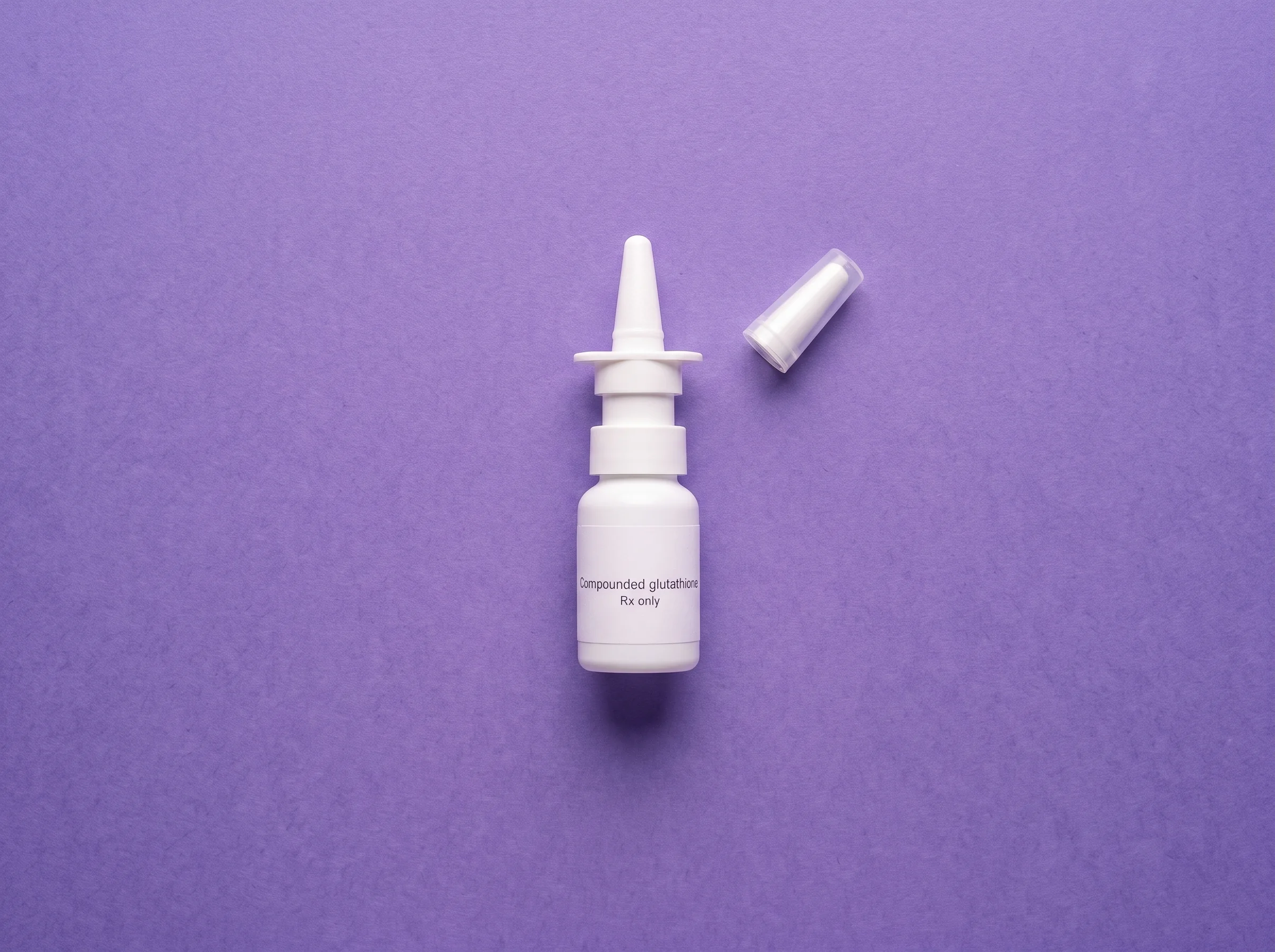 The Compounded glutathione sprayer bottle and its cap, laid out overhead on iris paper in the order they are used