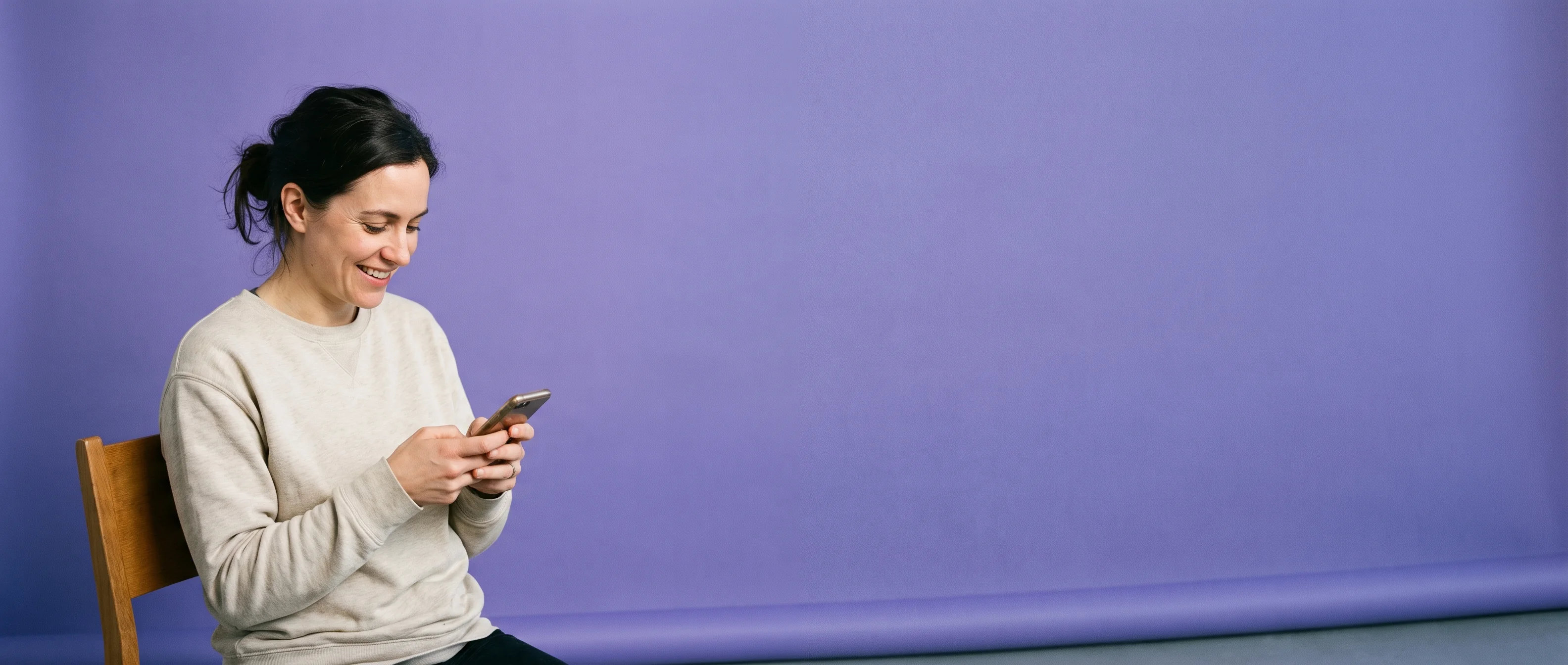 A woman perched on the arm of a chair reading her phone against iris paper