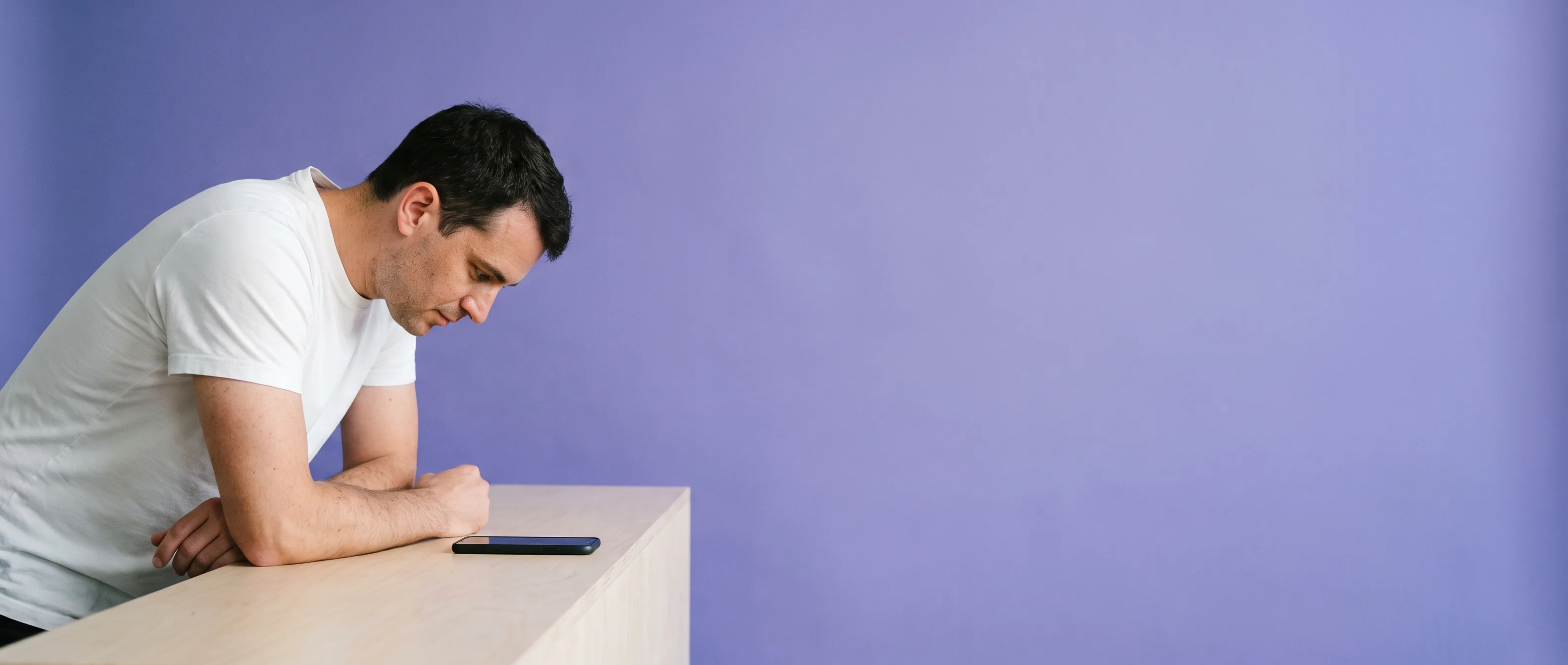 A man leaning on a counter reading a phone lying flat in front of him, iris paper