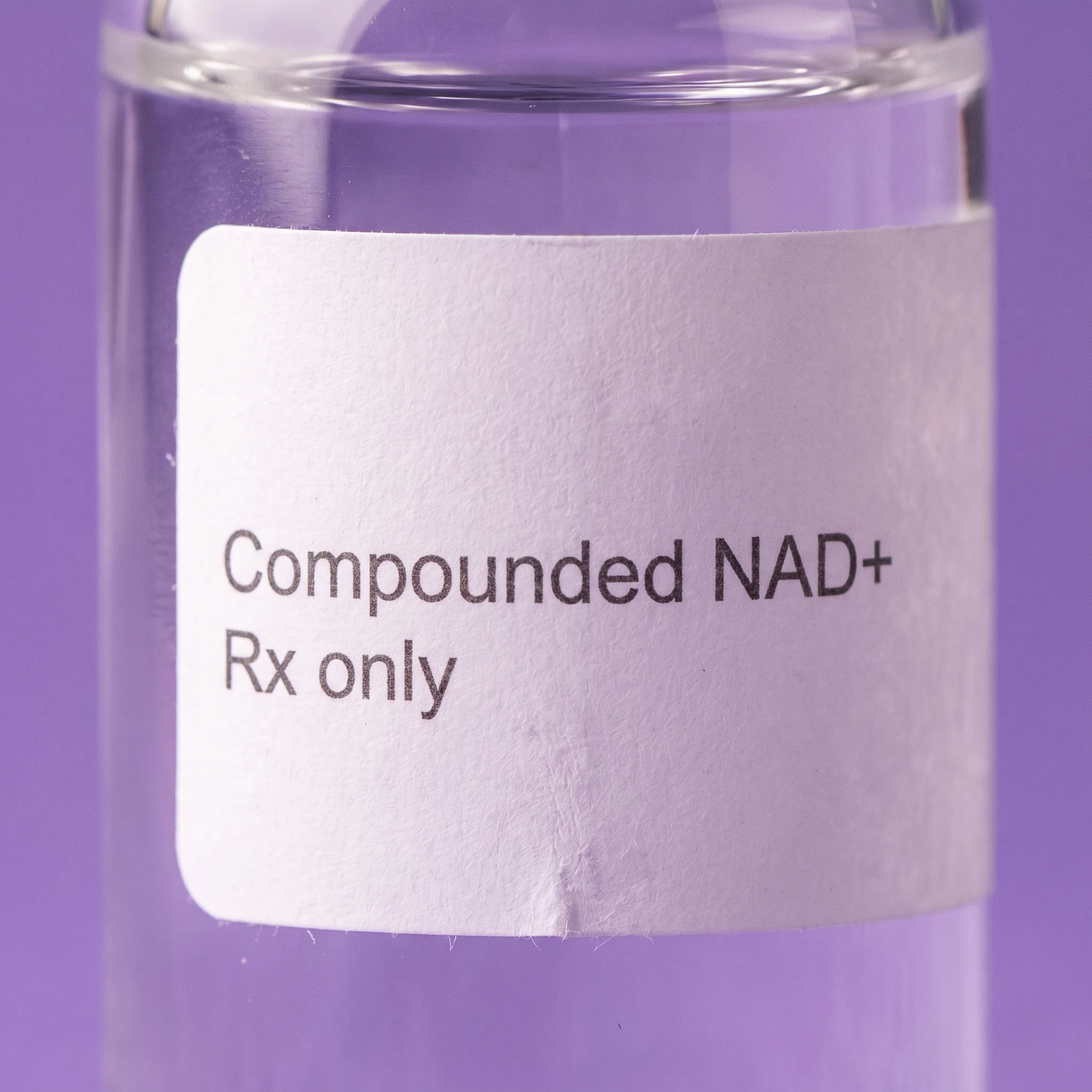 Macro detail of the plain white label, reading Compounded NAD+ above Rx only