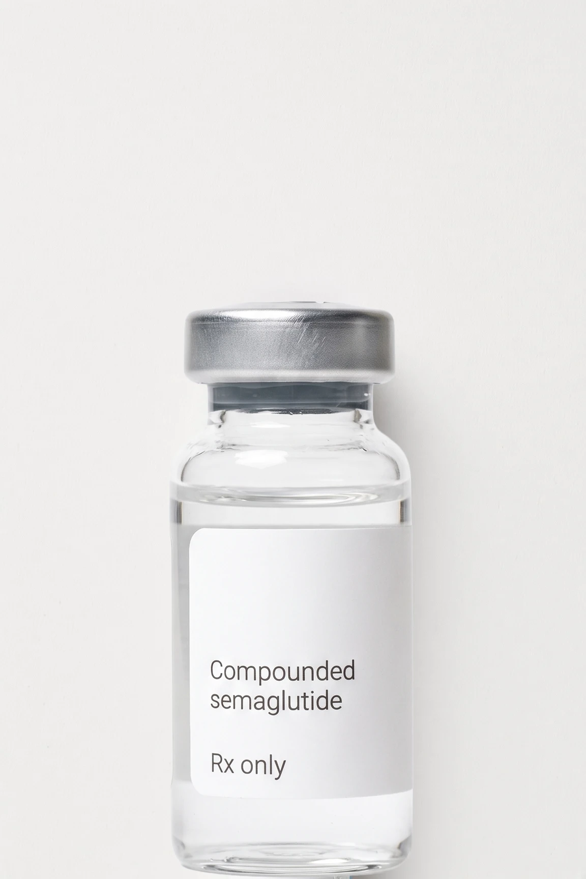 A vial of compounded semaglutide standing on a flat near-white ground