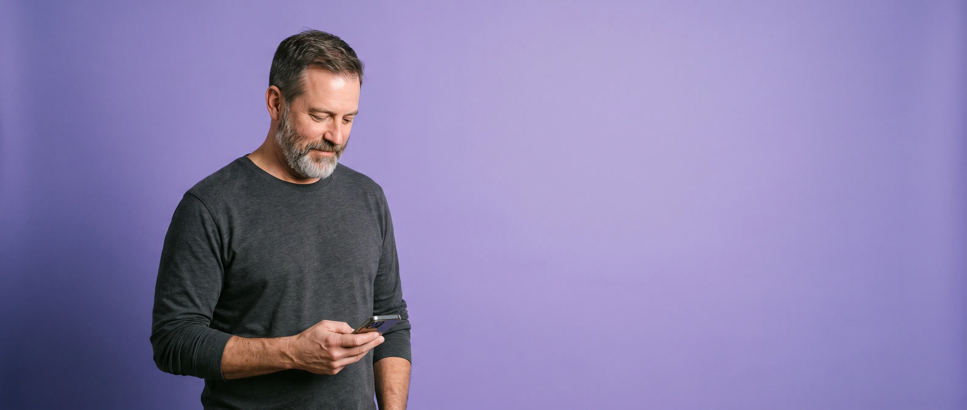 A man standing with his phone held low, glancing down at it, against iris paper