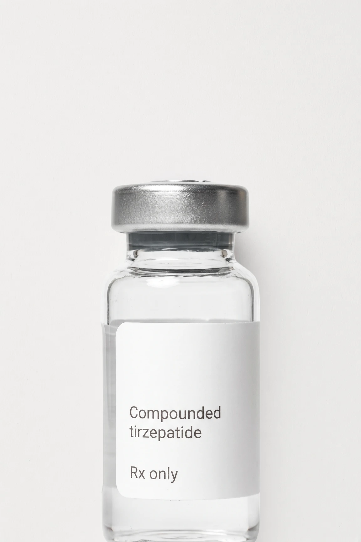A vial of compounded tirzepatide standing on a flat near-white ground