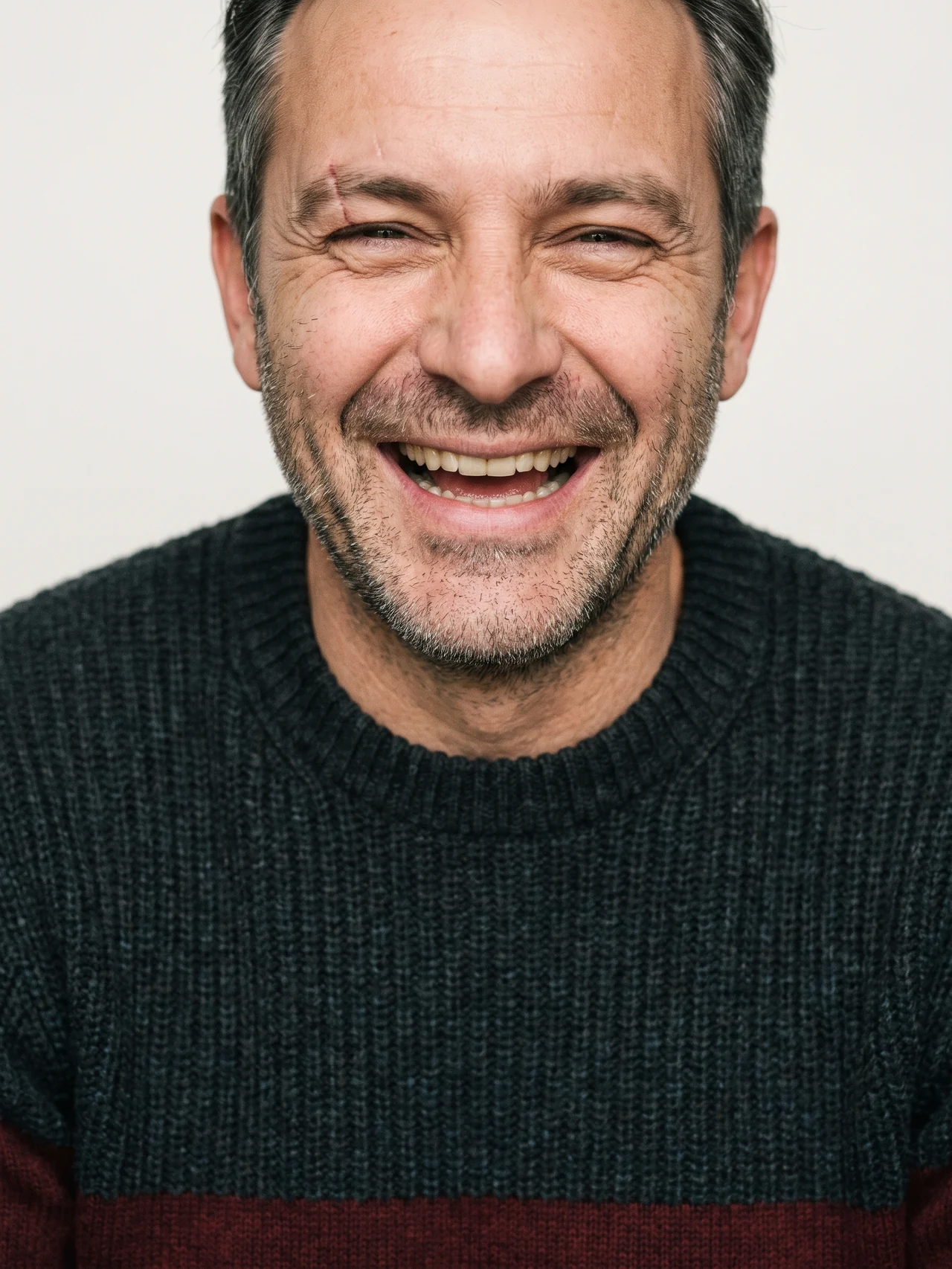 A man in his forties mid-laugh, cropped at the crown, against bone seamless paper