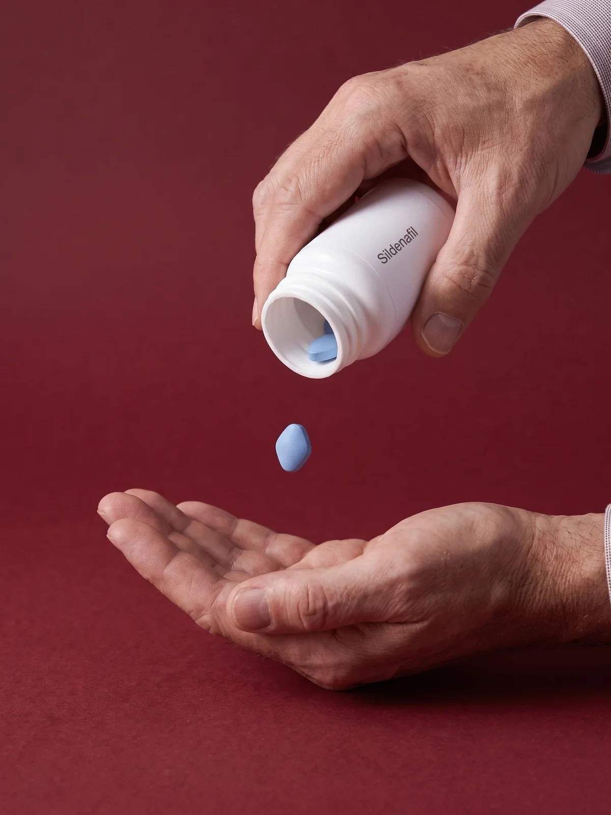 A hand tipping the bottle so one tablet falls toward an open palm below