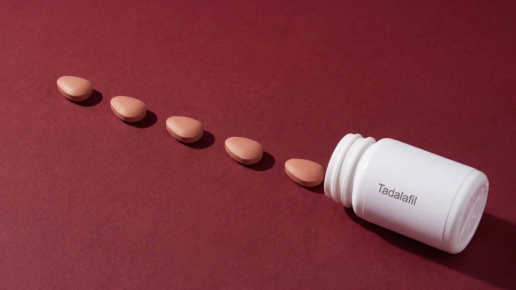 A plain white bottle labelled Tadalafil lying on oxblood paper, tablets running out of it in a diagonal