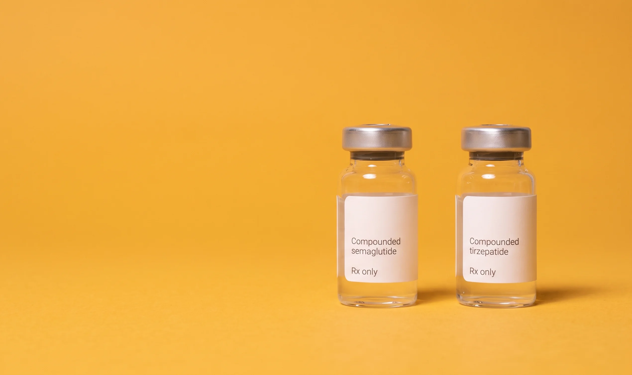 The compounded semaglutide and tirzepatide vials standing on flat amber seamless paper